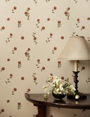 A console table with a table lamp sits in front of a wall covered with the Bamonte Textile String Floral Wallpaper by Jake Arnold