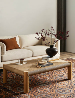 Lerner mahogany wood woven top coffee table styled with a cream colored sofa and orange geometric pattern area rug.