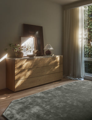 Damara solid viscose rug in sage styled with a modern geometric carved wood dresser.
