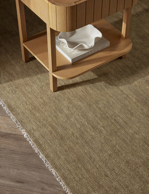 The Heritage moss gray rug lays under a rectangular side table with a book and white ruffle bowl in its shelf