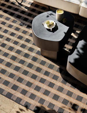 Armas black monolithic round outdoor side table by Sarah Sherman Samuel sitting a top a black and tan basketweave motif outdoor rug.