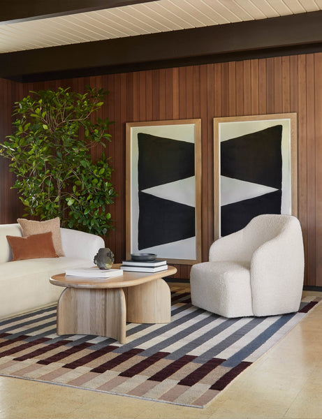 #showall::39840591577187 | The Tobi cream boucle swivel chair sits atop a striped rug in front of a wood paneled wall with two large geometric wall arts