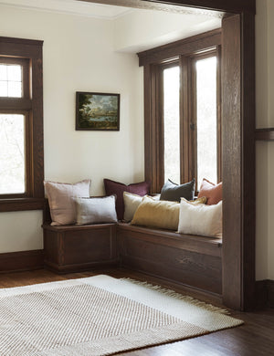 The Joelle rust rug lays in a nook with a wooden bench covered in different colored linen throw pillows