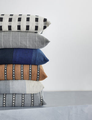 Bertu onyx black pillow with a woven dash pattern by Bolé Road Textiles sits at the top of a stack of Bole Road Textiles’ throw pillows