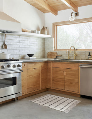 Elin mat lays on a gray floor in a kitchen with wooden cabinetry, stainless teal appliances, and a wooden beamed ceiling