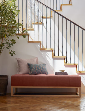 Tamra blue and pink lumbar pillow with floral patterns sits on a red linen bench in a room with a staircase in the background