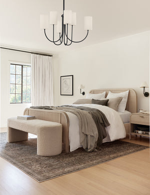 Amalia distressed traditional rug lays under a white-washed woven framed bed and a cream boucle bench