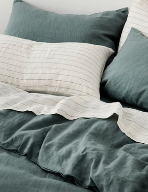 The set of two european flax linen bluestone pillowcases by cultiver lay on a bed with pencil stripe linens by cultiver