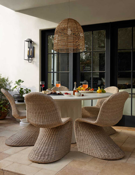 #color::vintage-white | The Manila wicker weave beige indoor and outdoor dining chair sits in a covered outdoor dining space beneath a natural jute chandelier surrounding an ivory circular dining table