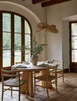 Four Nicholson slim natural oak wood frame and woven seat dining chair styled around an oval light wood dining table.