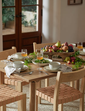 The Nature deep plate in sand by Thomas for Rosenthal sits on a wooden rectangular dining table in a dining room with woven-base dining chairs and long stemmed wine glasses