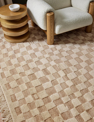 The Irregular Checkerboard Rug by Sarah Sherman Samuel sits in a living room with a retro wooden four tiered side table and a white boucle rounded accent chair.