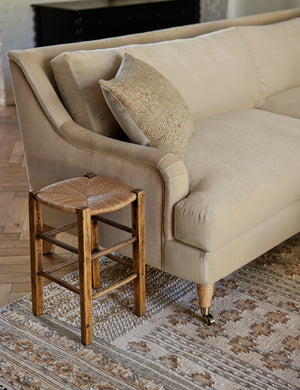  The Rivington brie beige velvet sofa sits atop a patterned rug next to a stool with a woven base