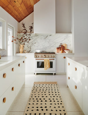 The irregular dots rug in its runner sizes lays in a kitchen with white cabinetry, a brass stove, and sloped wooden-paneled ceilings