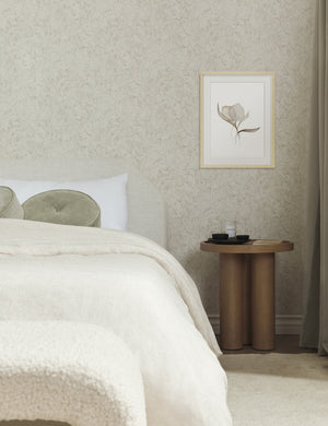The Pale Bouquet Print hangs in a bedroom above a circular side table next to a natural linen framed bed with ivory linens