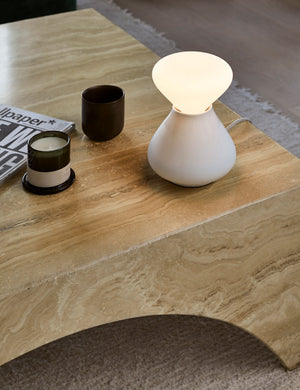 The Reflection Noma white table lamp by Tala sits atop a natural wooden coffee table with two black candles atop a natural woven rug