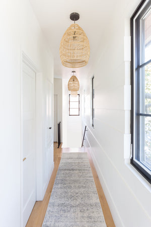 The Prisha bohemian style distressed stone gray rug lays in a bright hallway with black framed windows and woven pendant lights