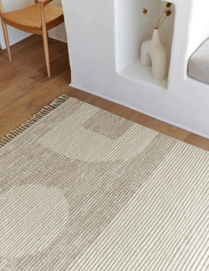 Close-up of the Nomad neutral-toned geometric floor rug by Élan Byrd with subtle ribbed design in a room with a sculptural white vase and a neutral wooden dining table atop hardwood floors