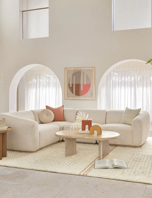 The Rina wool moroccan rug sits in a bright living room with a rounded white sofa, a light wooden coffee table, and orange and yellow sculptural decor