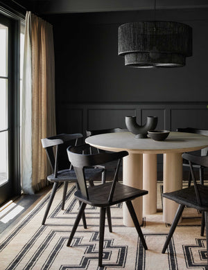 The Damien half-circle sculpture vase by Ateriors with matte black glaze finish sits in a dark dining room with black accented walls, black dining chairs, and a black and beige geometric rug