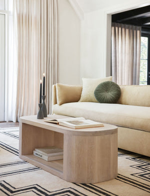 The Monroe moss green velvet round pillow sits on a natural sofa in a living room with an oval coffee table and geometric rug