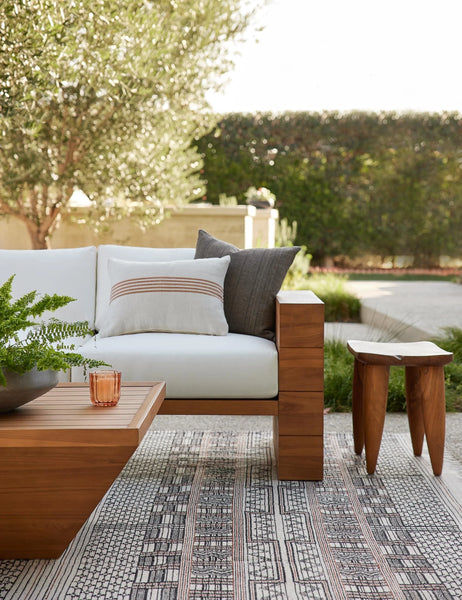#color::rust-stripe #style::lumbar | Katya Indoor and Outdoor lumbar cream Pillow with rust brown stripes in the center sits on a white cushioned coach outside next to a gray pillow